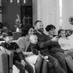 A happy family of six enjoying a cozy time together at home in a monochrome setting.